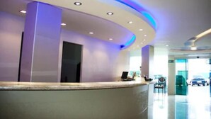 A reception area with a curved reception desk, a seating area, and a glass door leading outside. - Emirates Hotel & Suítes (Santana do Livramento)