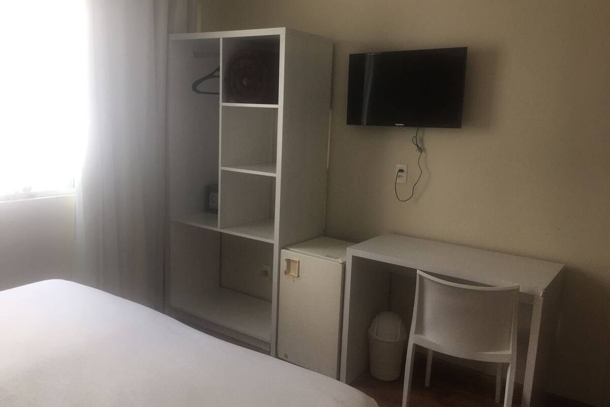 Hotelkamer met een bed, een wit bureau, een stoel, een aan de muur bevestigde televisie en een garderobe met meerdere planken.