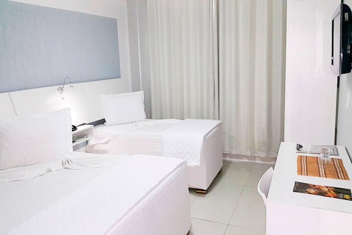 Een hotelkamer met twee bedden, een bureau, een televisie en een raam met gordijnen.