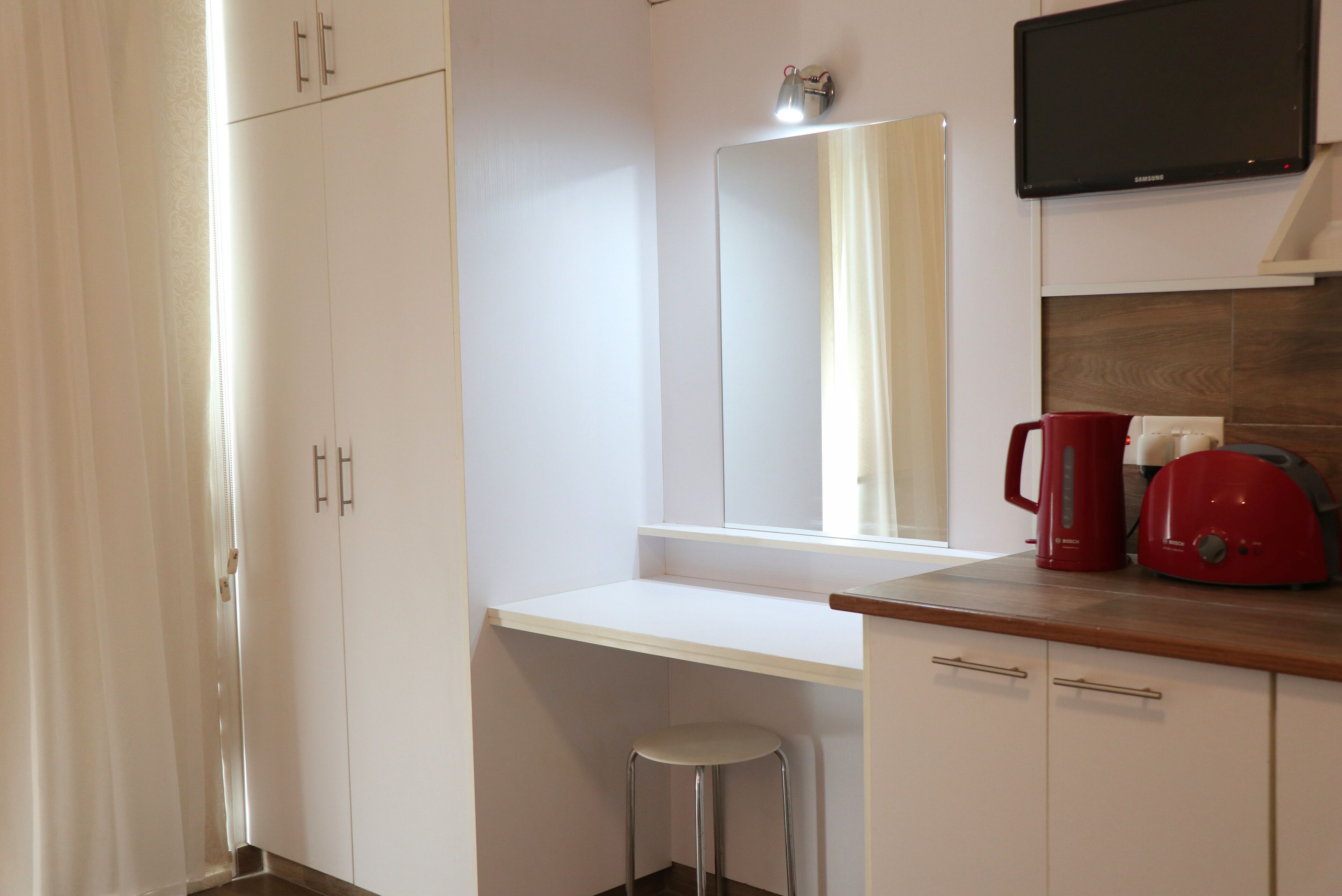 Una cucina moderna con mobili bianchi, un piano di lavoro in acciaio inossidabile, un bollitore rosso e una TV a schermo piatto montata sopra il bancone.