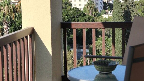 A balcony with a view of the sea and buildings, a table with a bowl, and a chair. - Layiotis Hotel Apartments (Larnaca)