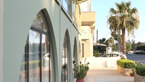 A building with large arched windows and a flat roof. There are potted plants on the sidewalk in front. - Layiotis Hotel Apartments (Larnaca)