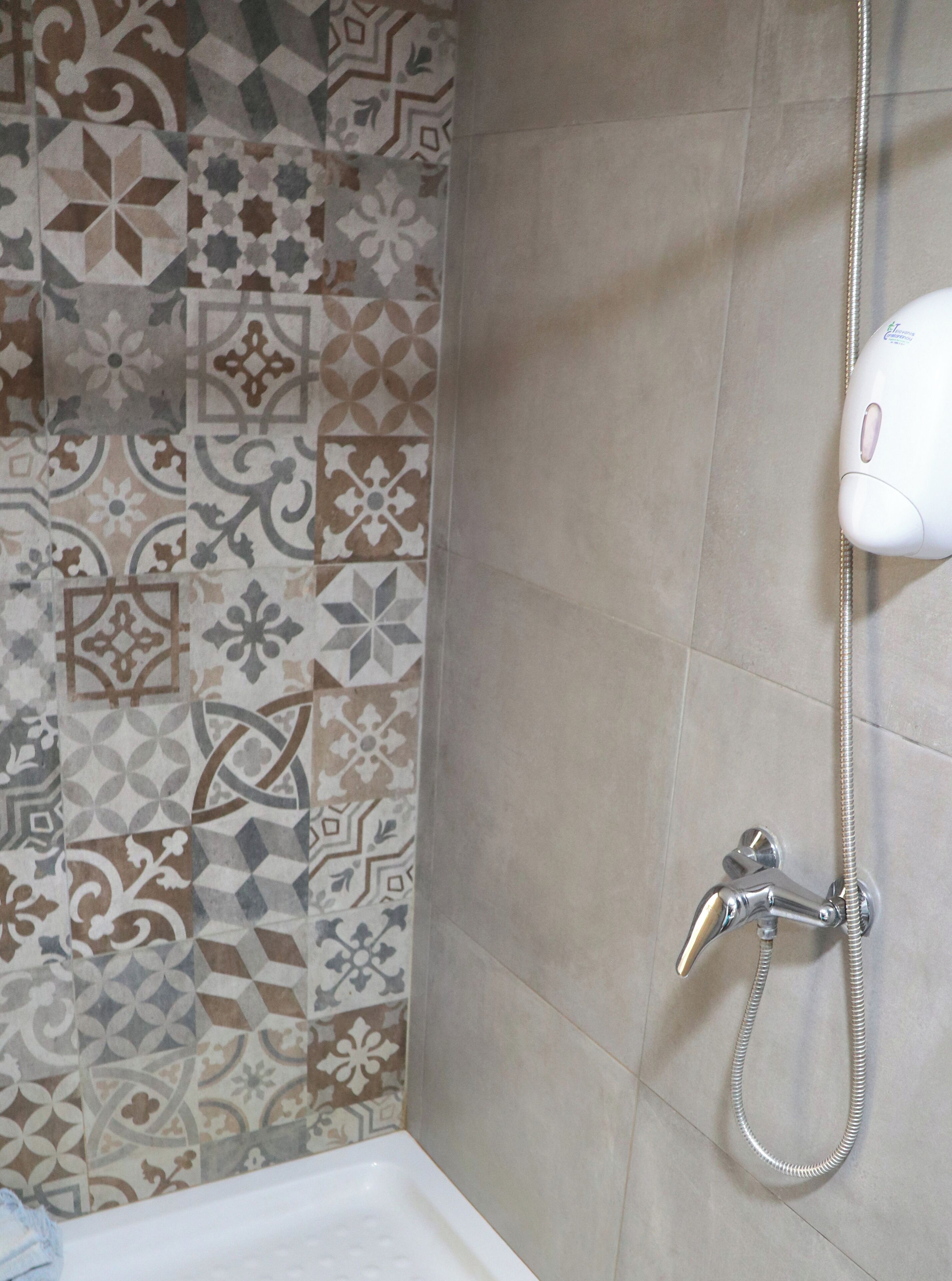 A bathroom with patterned tiles on the walls, a shower with a handheld showerhead, and a white bathtub.