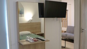 A hotel room with a bed, a desk with a mirror, a flat-screen TV mounted on the wall, an air conditioning unit, and a small stool. - Layiotis Hotel Apartments (Larnaca)