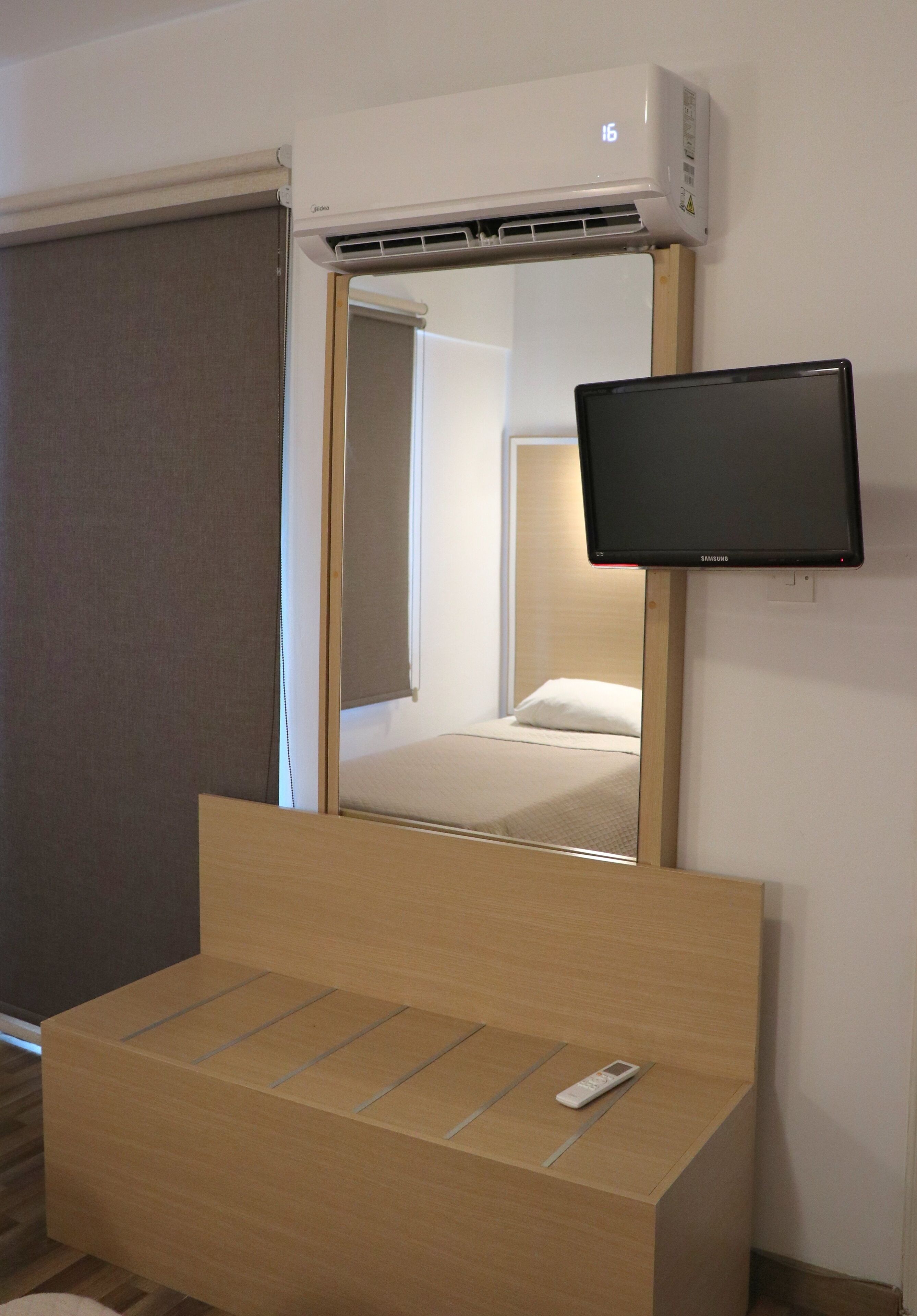 A hotel room with a bed, a TV mounted on the wall, and an air conditioning unit above the bed.