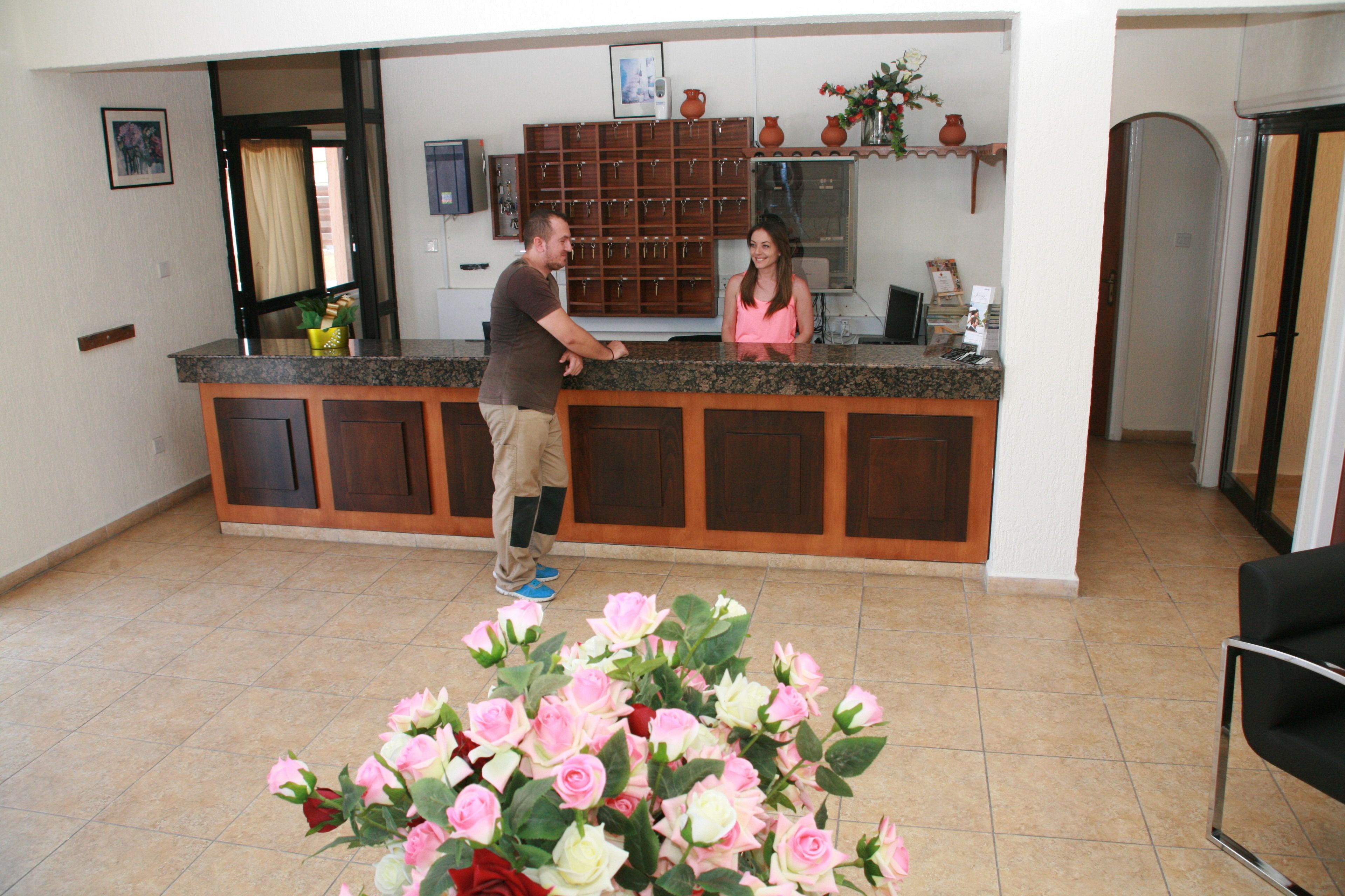 A reception area with a counter, a man and a woman standing, and a large floral arrangement in the foreground.