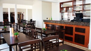 A restaurant with multiple wooden tables and chairs, a bar area with shelves of glasses, and a menu stand. - New York Plaza Hotel Apartments (Paphos)