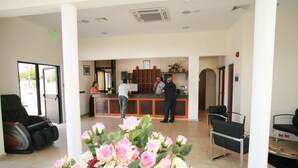 A reception area with a counter, chairs, and a massage chair. - New York Plaza Hotel Apartments (Paphos)