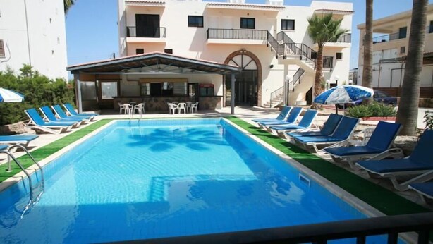 A swimming pool with lounge chairs and a covered seating area. - New York Plaza Hotel Apartments (Paphos)