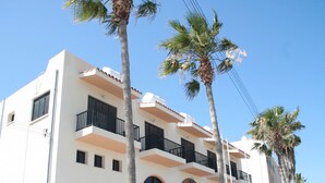 A multi-story building with balconies, palm trees, and a clear blue sky. - New York Plaza Hotel Apartments (Paphos)