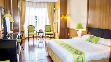 Camera d'albergo con un letto grande, due poltrone, un tavolino, una scrivania con lampada e una finestra con tende.