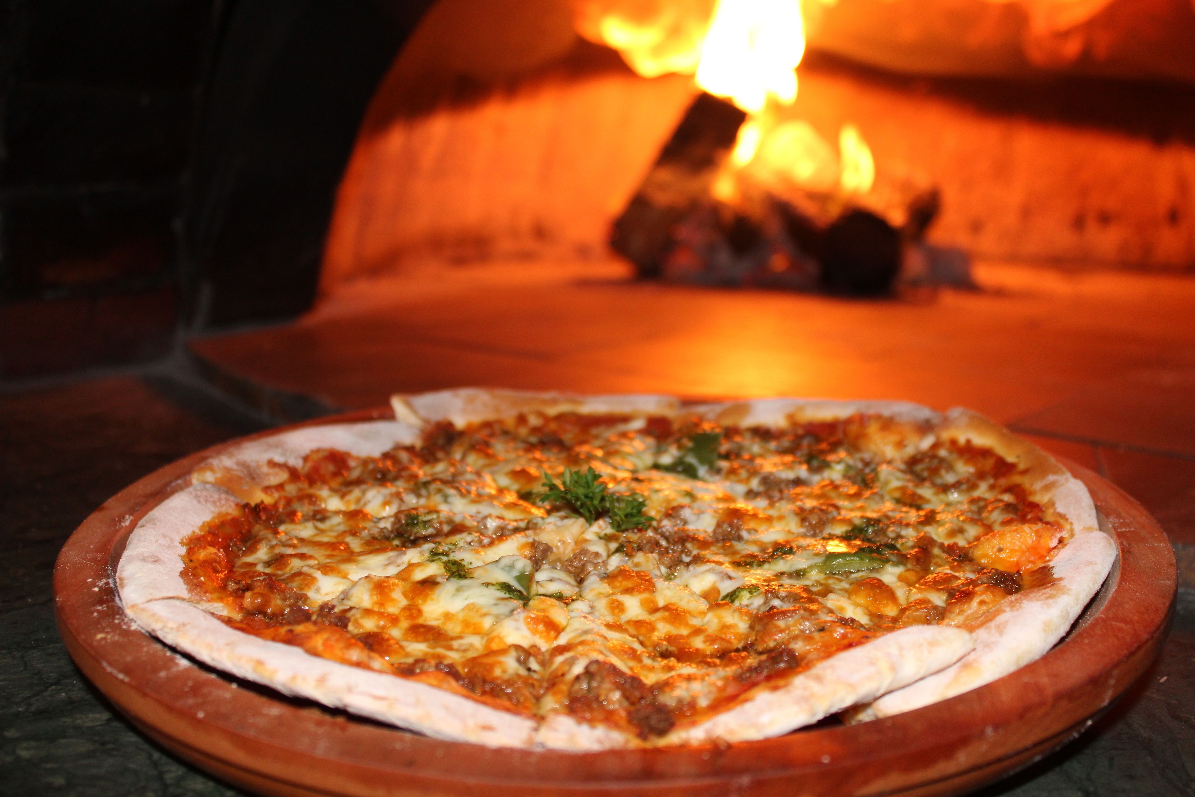 Une pizza cuite dans un four à bois, où l’on peut voir les flammes.
