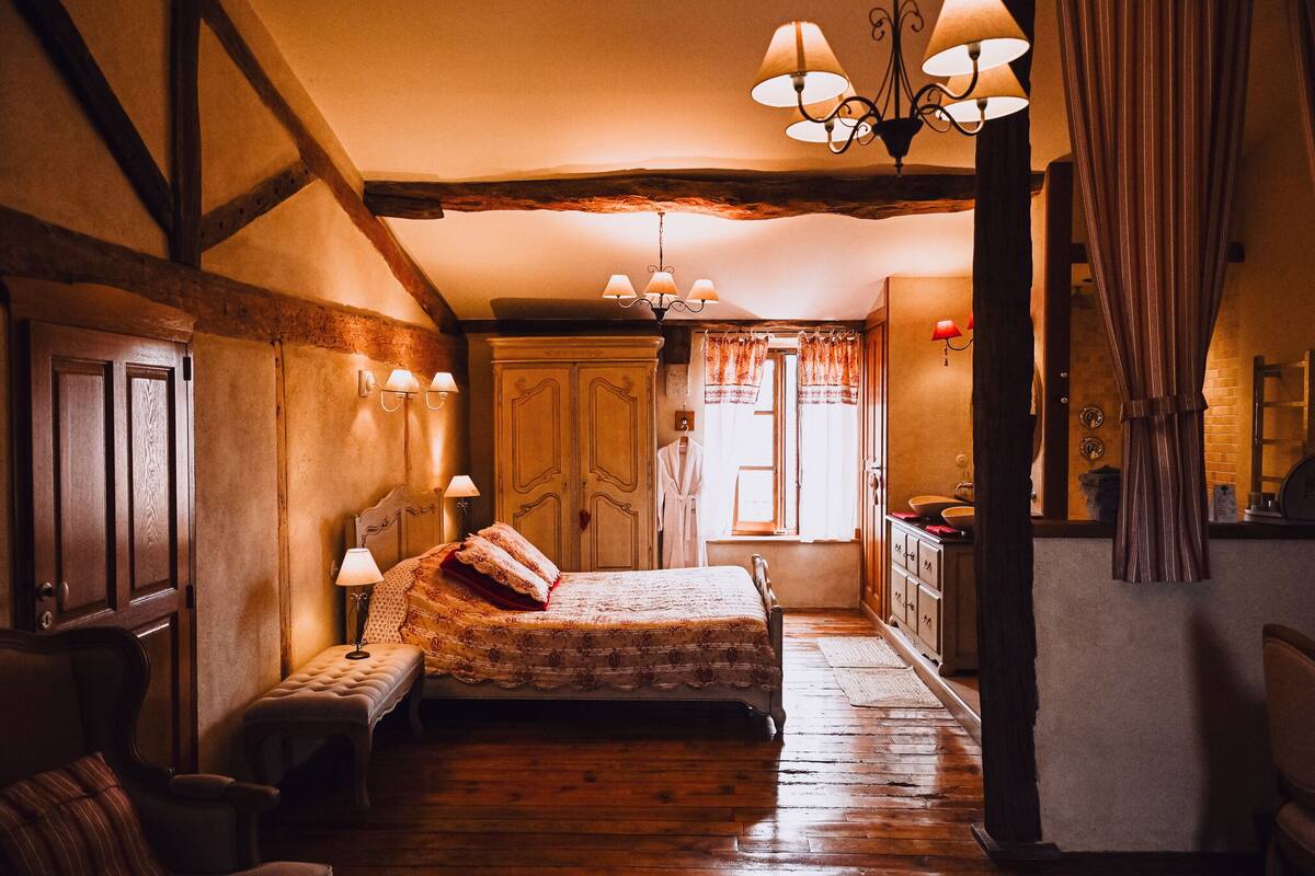 A traditional bedroom with a wooden bed, a bench, a dresser, and a window with curtains.