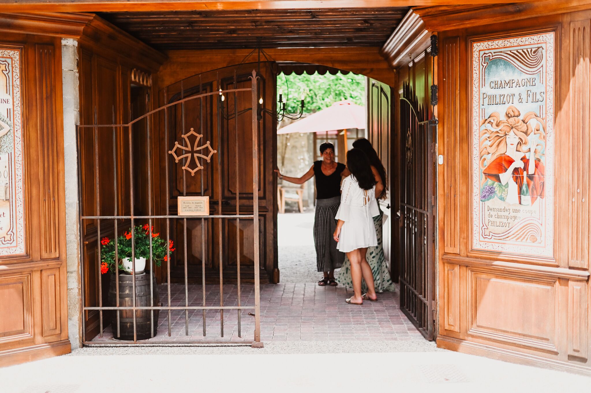 A wooden entrance with a metal gate, a potted plant with red flowers, and a poster on the wall.