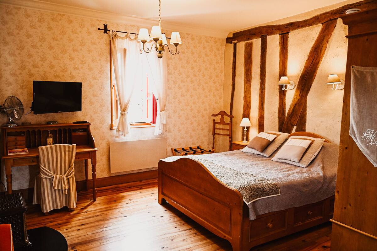 A bedroom with a wooden bed, a desk with a television, and a chair.
