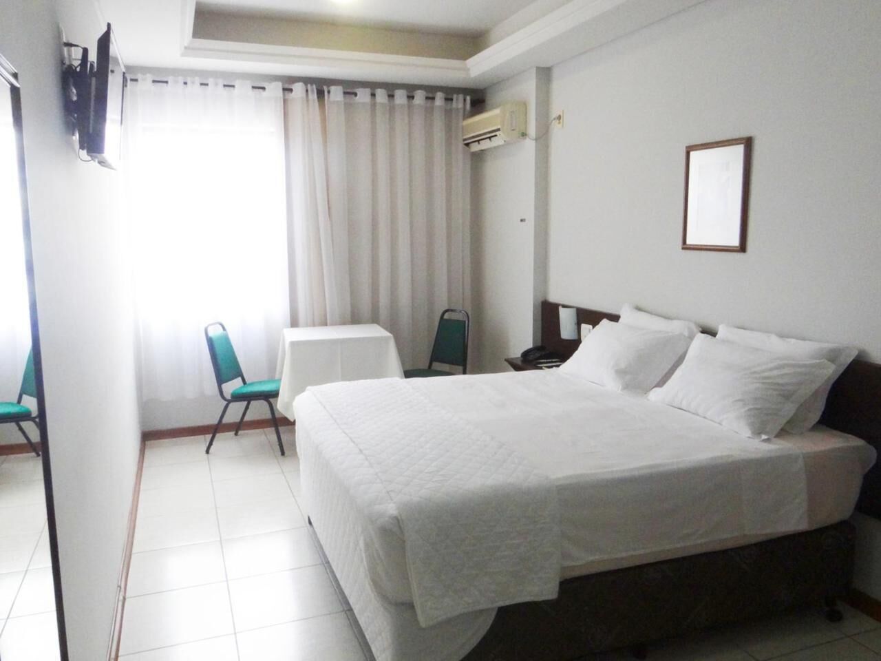 A hotel room with a bed, a chair, a small table, and a window with curtains.