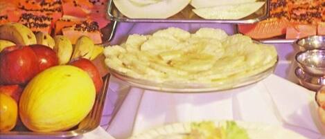 Un buffet proposant une variété de fruits et de légumes, notamment des pommes, des oranges et un melon.