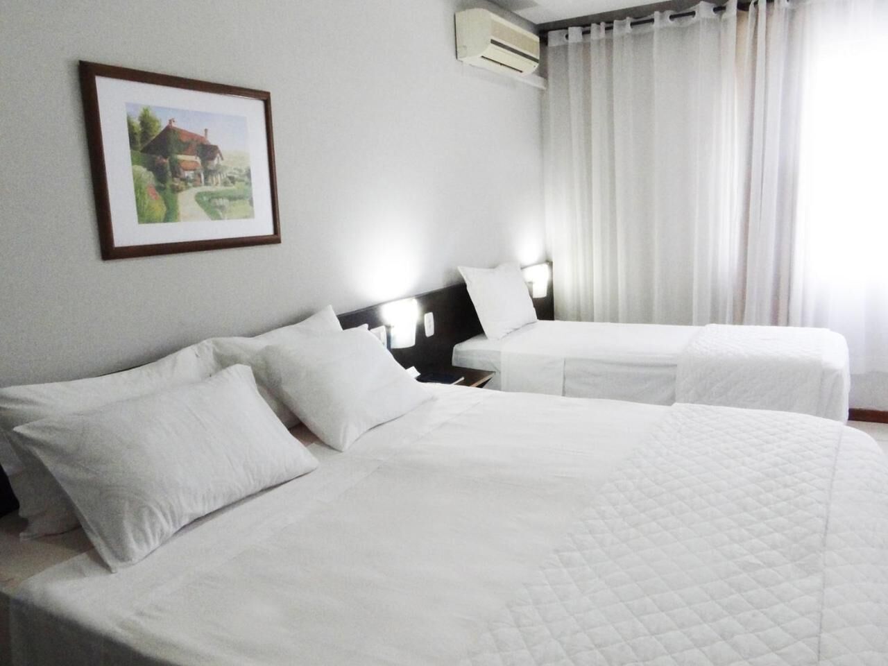 Habitación de hotel con dos camas, ropa blanca de cama, un cuadro en la pared y un equipo de aire acondicionado.