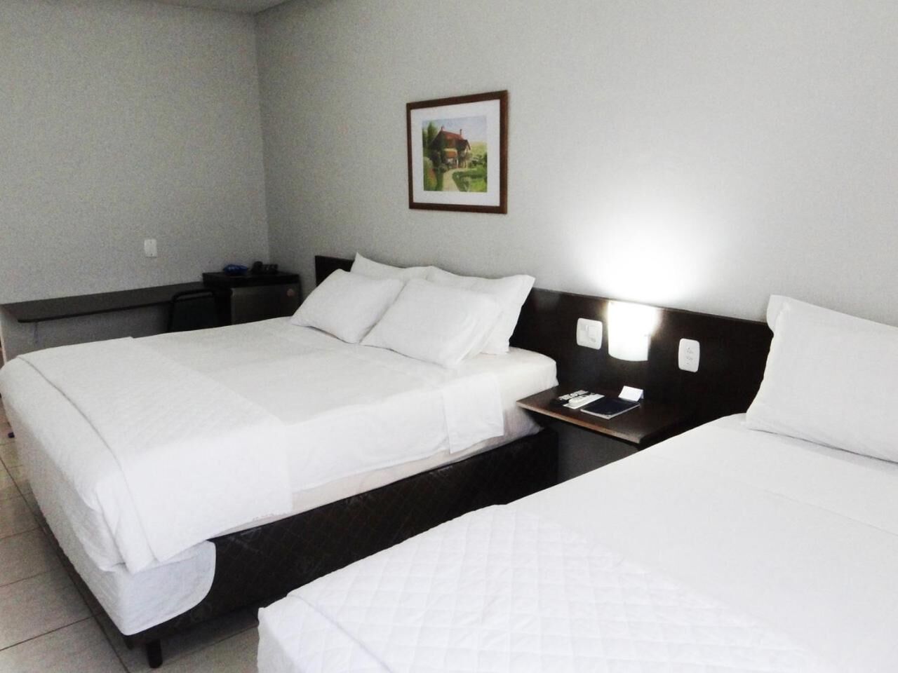 A hotel room with two beds, a nightstand, and a framed picture on the wall.