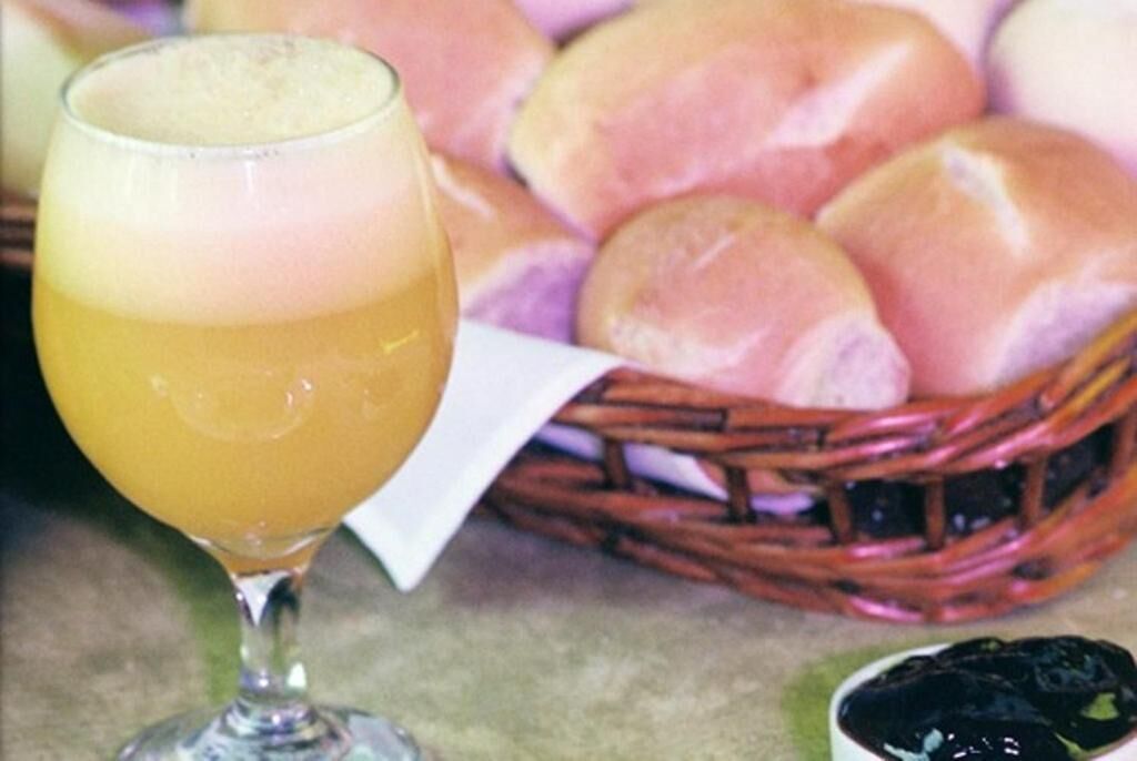 A glass of orange juice and a basket of rolls.