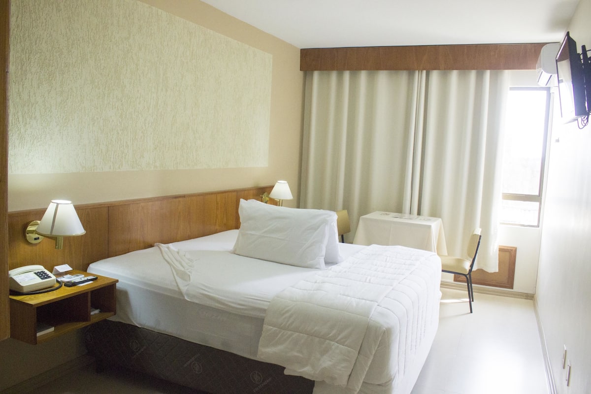 Une chambre d’hôtel avec un lit bien fait, des lampes de chevet, un téléphone et une petite table avec une lampe.