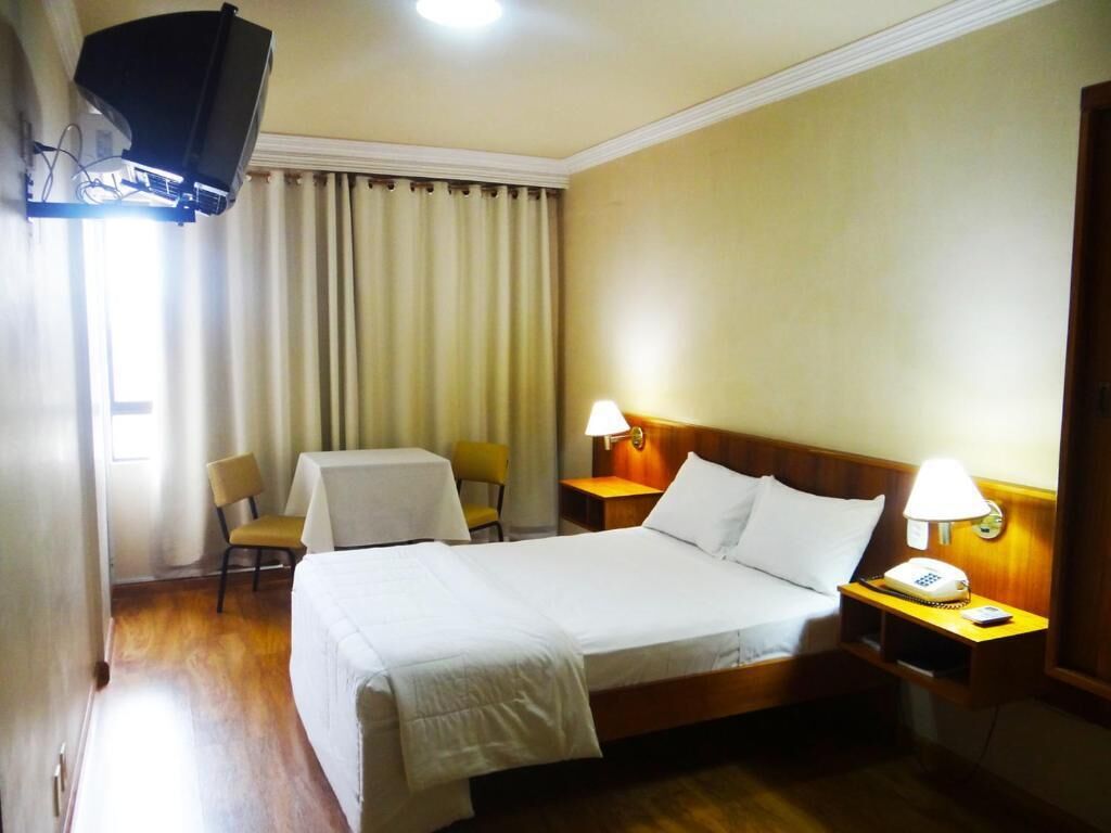 Een hotelkamer met een bed, nachtlampjes, een telefoon, een stoel en een tafel.