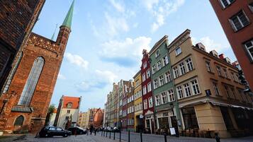 A cobblestone street lined with colorful historic buildings, a prominent church tower, and parked cars.