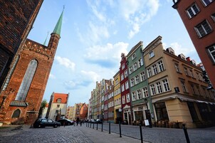 Una calle empedrada bordeada por edificios históricos coloridos y una imponente torre de iglesia, con coches estacionados.