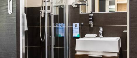 Ein modernes Badezimmer mit einer ein Glasfachwerk-eingeschlossenen Dusche, einem weißen Waschbecken und einem Spiegel darüber.