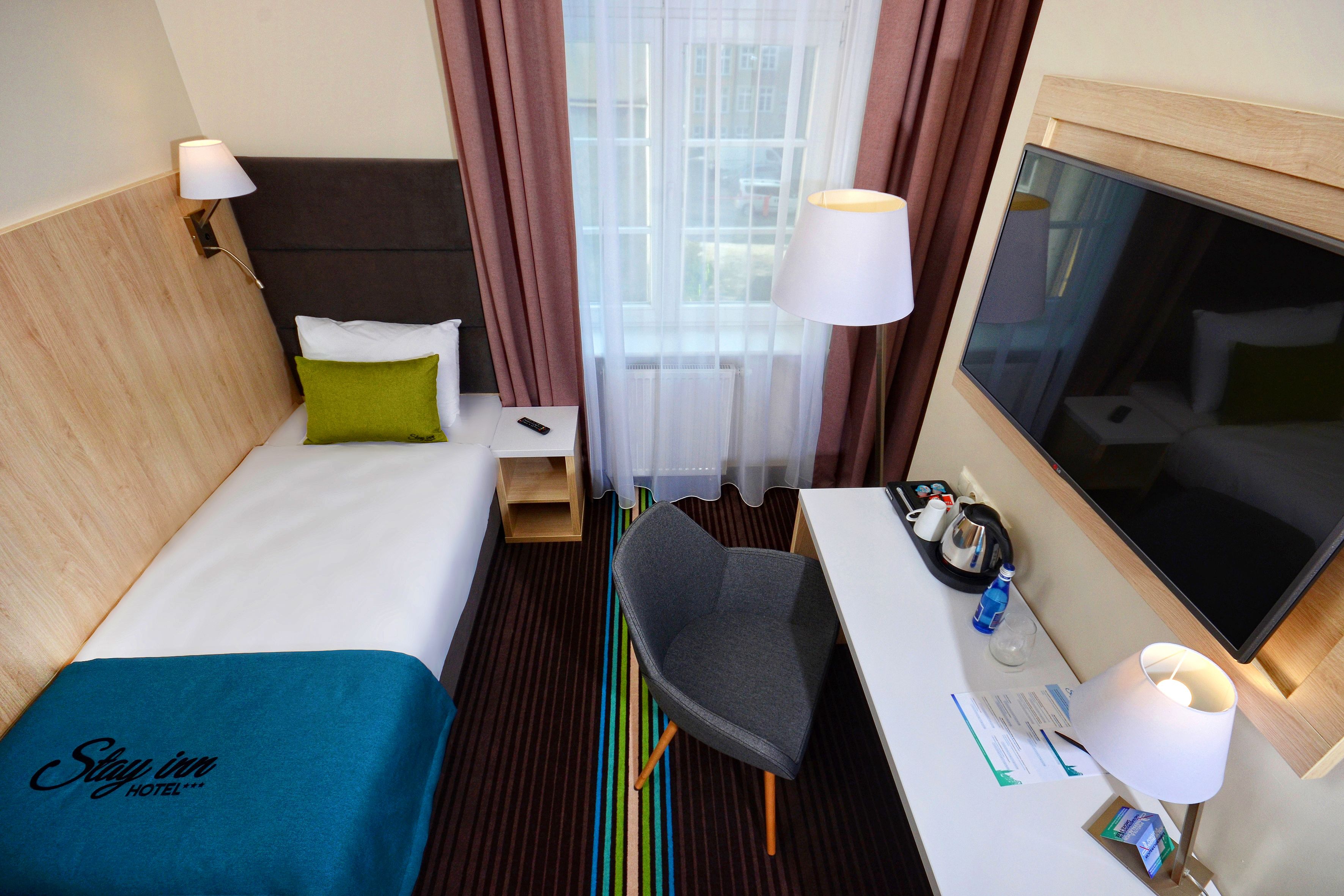 A hotel room with a bed, a desk, a chair, a TV, and a window with curtains.