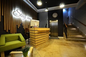 A reception desk with a clock, a staircase, and a green sofa in a modern lobby.