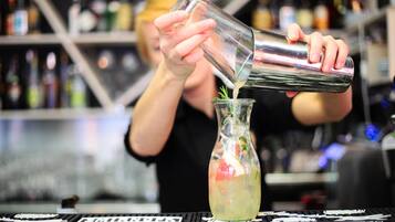 Un barman verse une boisson dans un verre, en y ajoutant une branche de romarin.