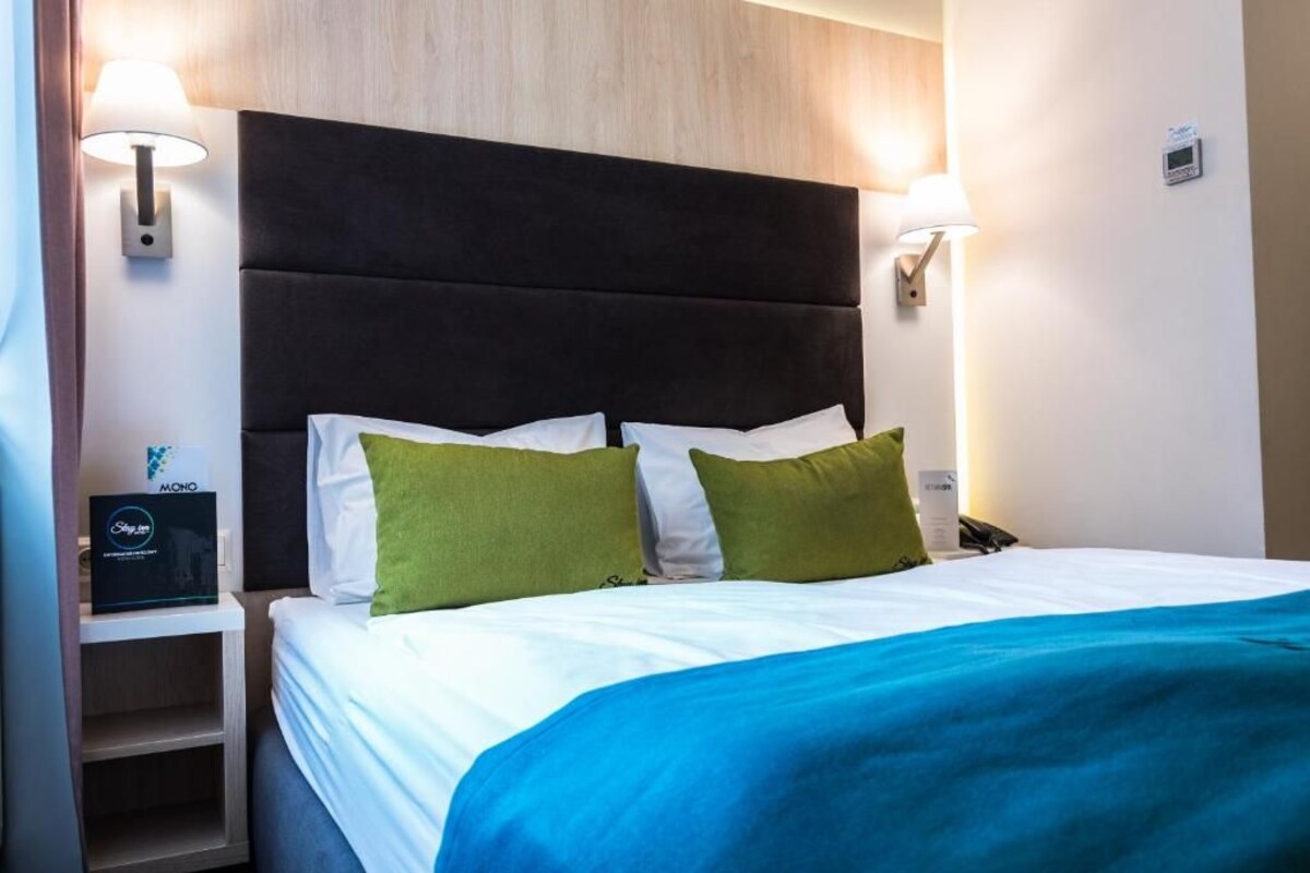 A hotel room with a large bed, two pillows, a nightstand with a lamp, and a control panel.