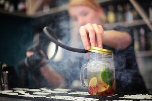 A person pouring a drink from a jar with a gold lid, surrounded by smoke.
