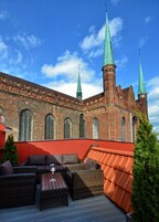 A historic building with a brick facade, multiple arched windows, and three prominent green spires.