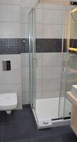 A modern bathroom with a glass-enclosed shower, a white toilet, and a towel rack.