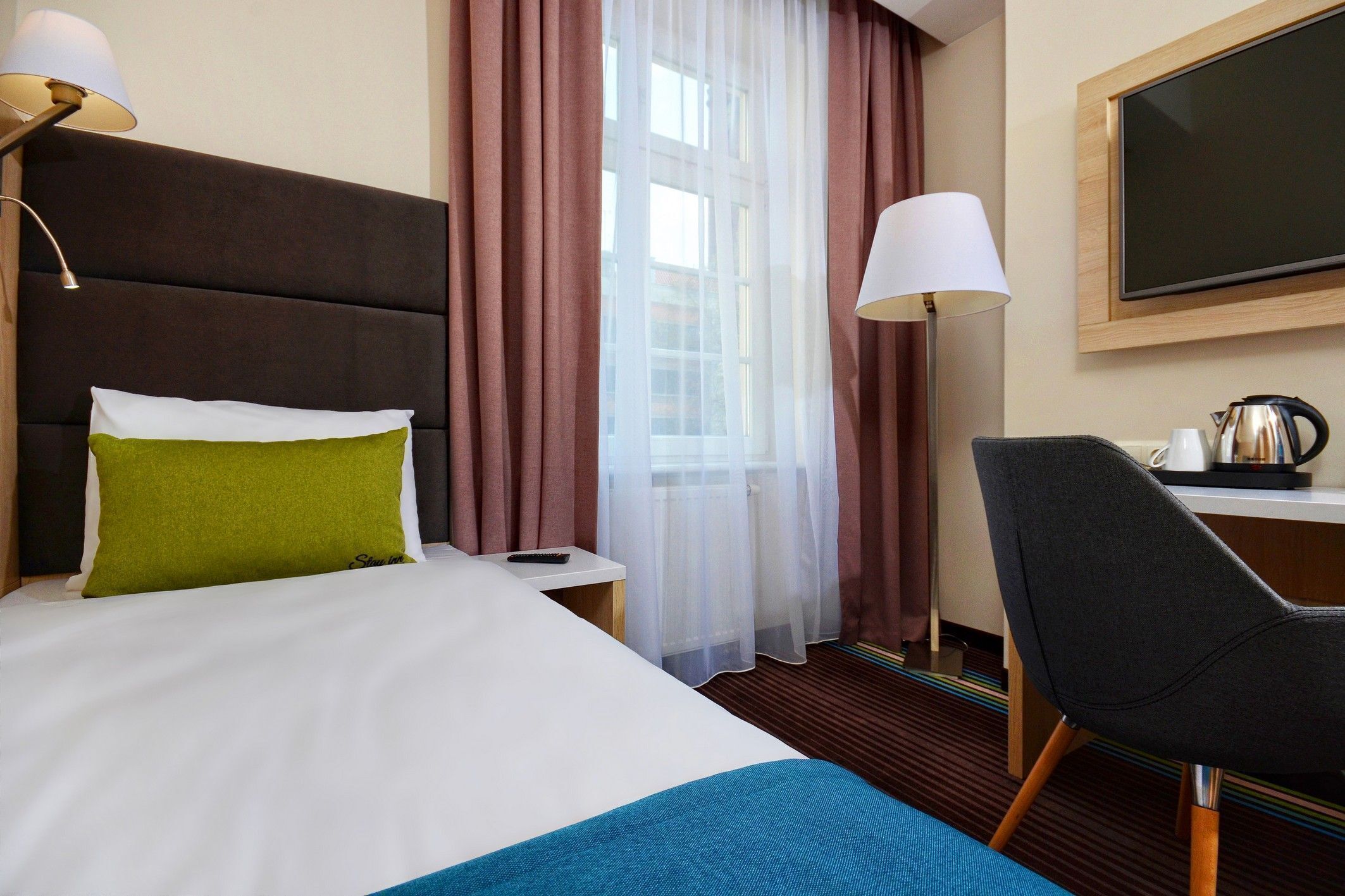 Een hotelkamer met een bed, een bureau, een stoel, een televisie en een raam met gordijnen.