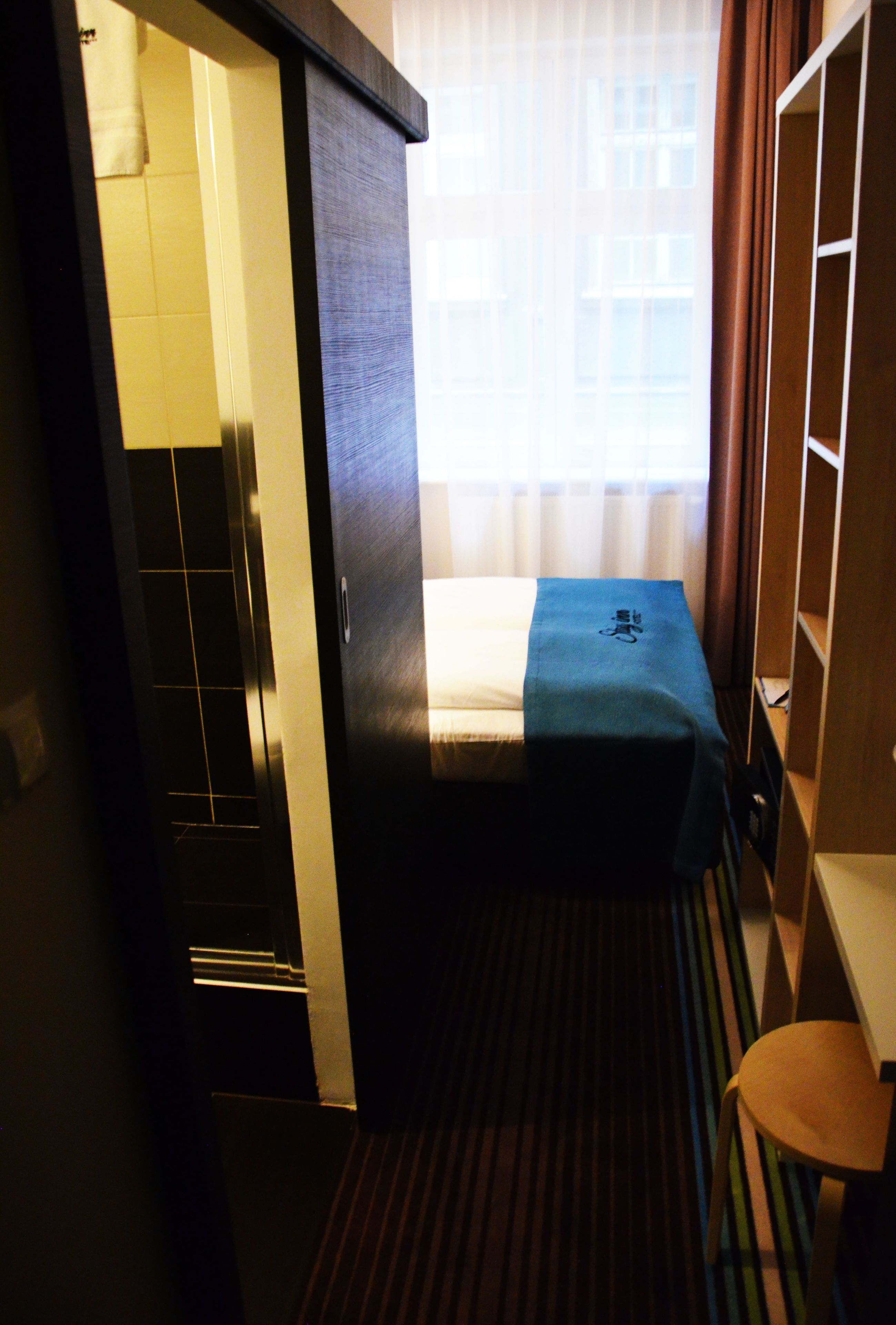 A compact hotel room with a bed, a small table, and a wardrobe.