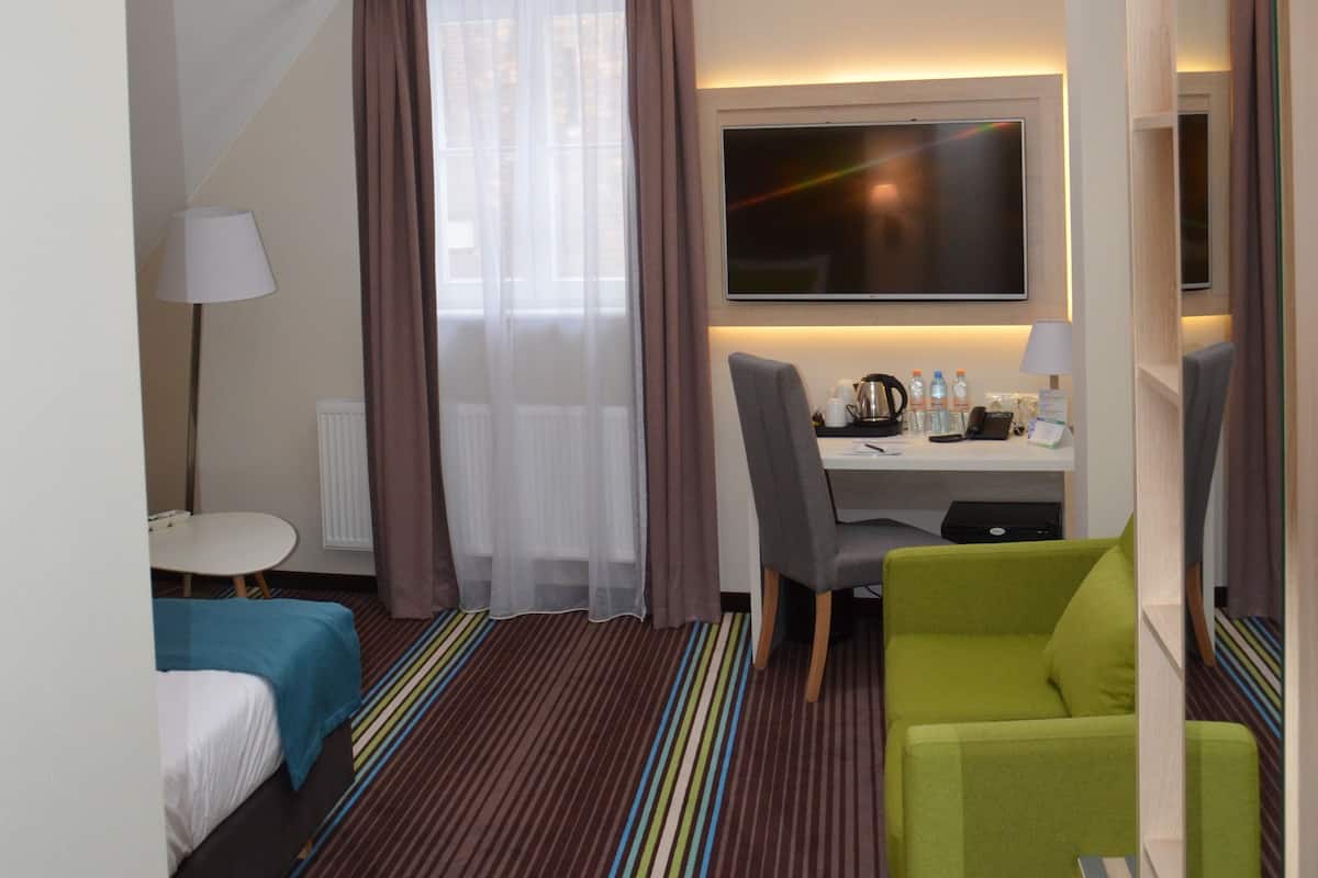 A hotel room with a bed, a desk, a TV, a chair, and a large window with curtains.