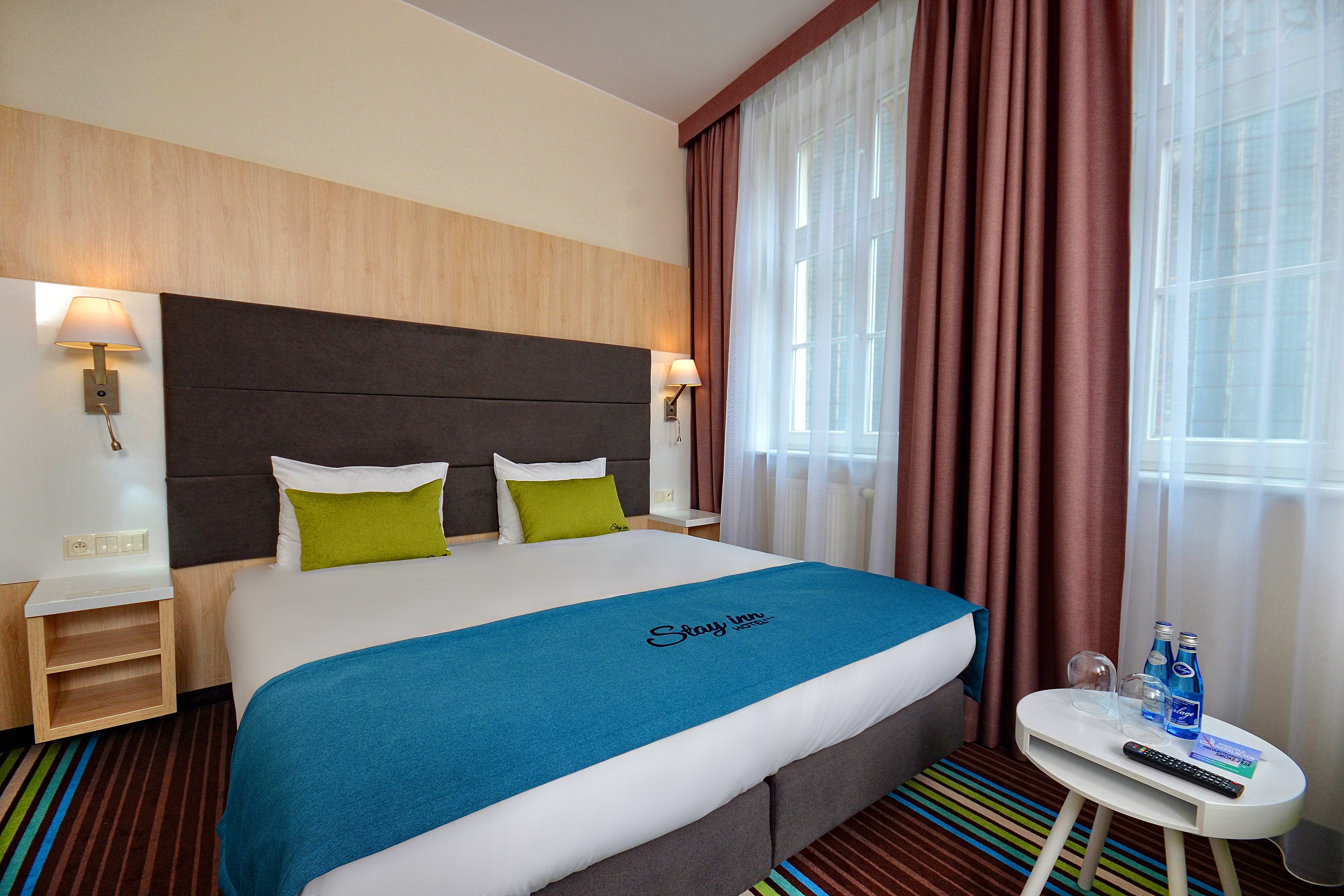 Habitación de hotel con cama, mesita de noche, cortinas en la ventana y alfombra a rayas.