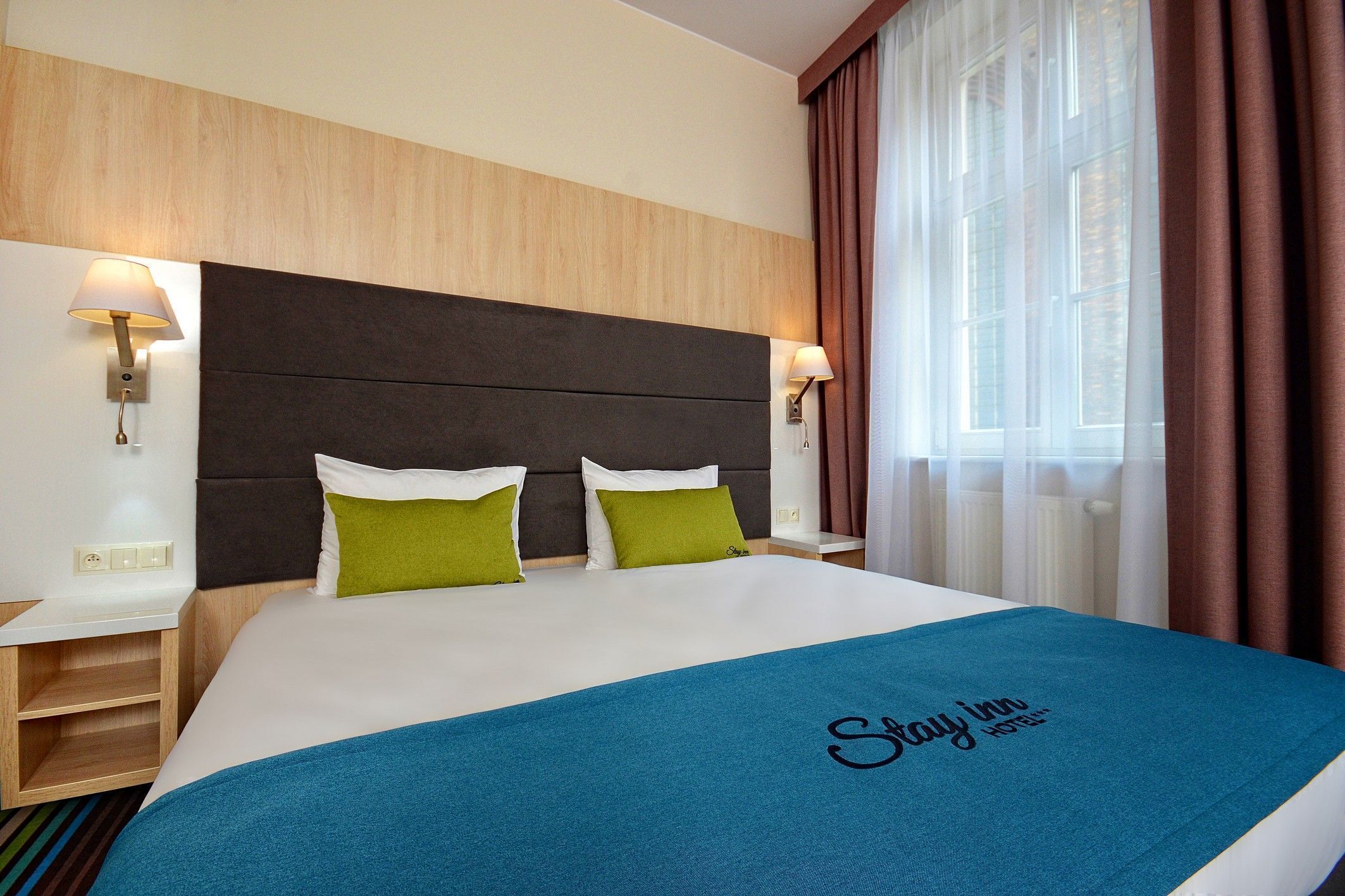 A hotel room with a large bed, two pillows, a blue blanket, and a headboard.