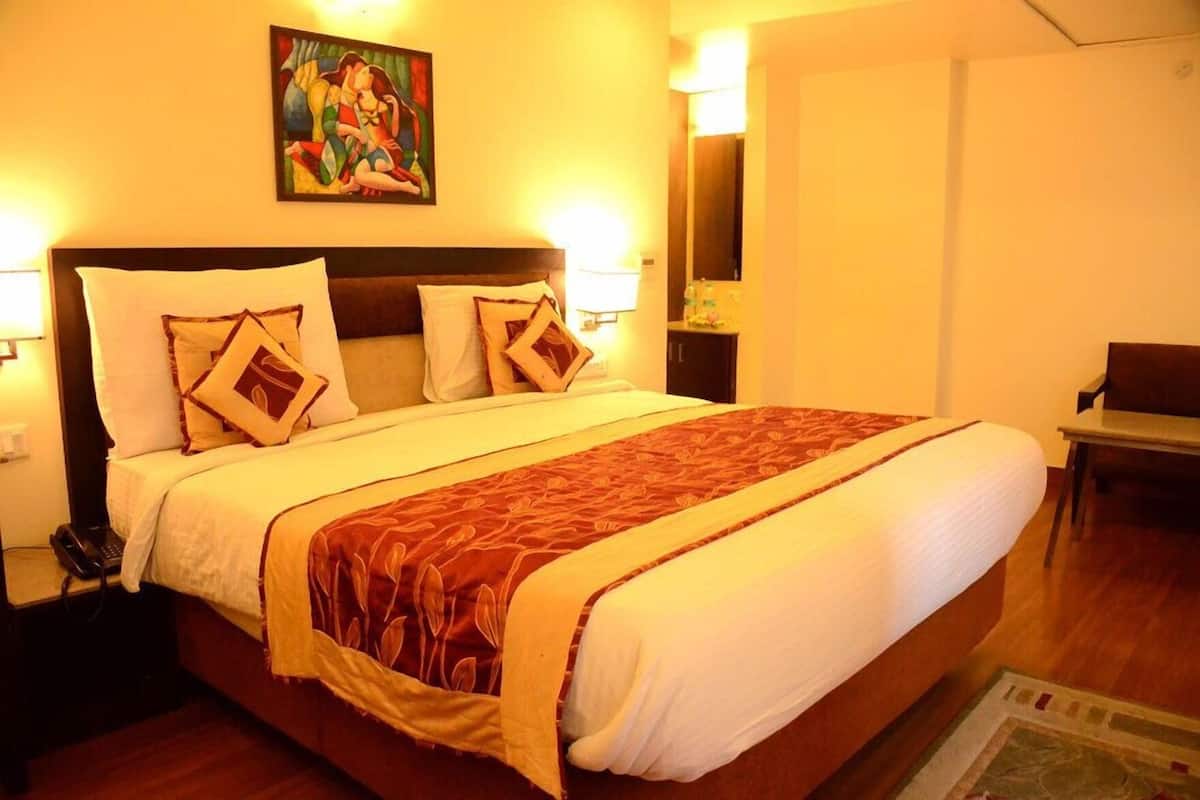 A hotel room with a large bed, bedside lamps, a painting on the wall, and a desk with a chair.