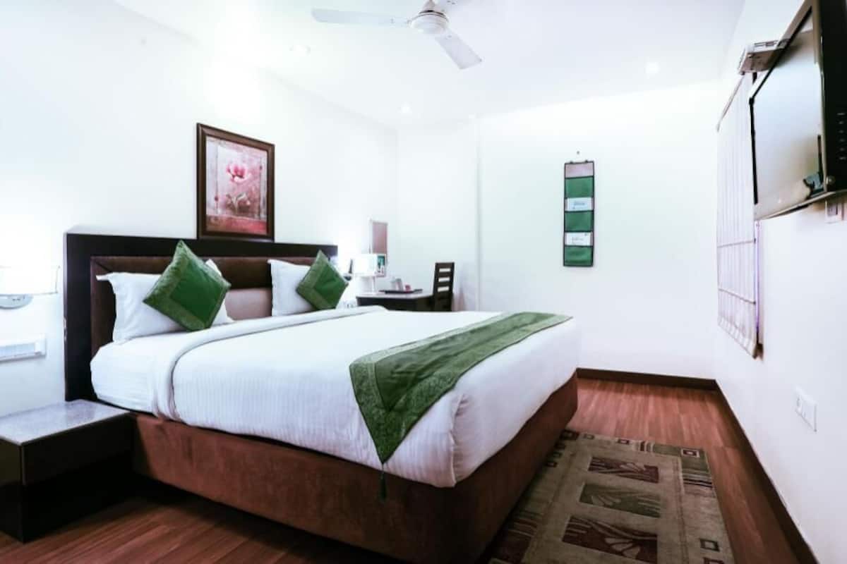 A bedroom with a bed, nightstand, wall-mounted TV, and a ceiling fan.