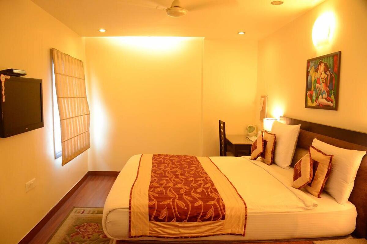 A hotel room with a bed, a desk, a chair, a painting on the wall, and a ceiling fan.