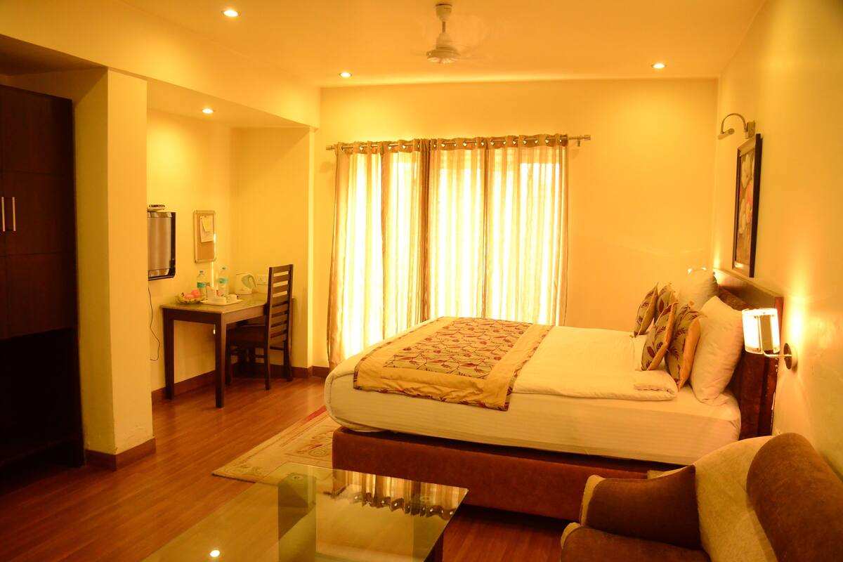 A hotel room with a bed, a desk, a chair, and a glass table.