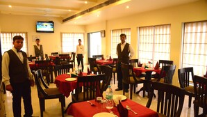 Un restaurante con varias mesas, cada una cubierta con manteles rojos, y un televisor montado en la pared.