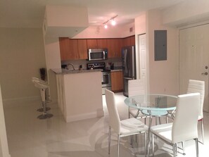 A modern kitchen with wooden cabinets, stainless steel appliances, and a glass dining table with white chairs. - LYX Suites at Merrick Park in Coral Gables (Coral Gables)