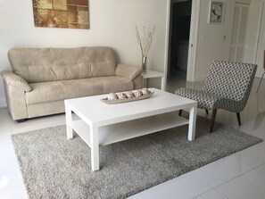 A living room with a beige sofa, a white coffee table, a patterned armchair, and a vase with dried plants. - LYX Suites at Merrick Park in Coral Gables (Coral Gables)