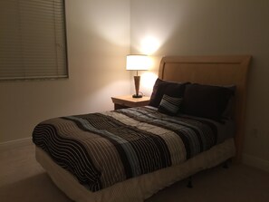 A neatly made bed with striped bedding, a bedside lamp, and a wooden headboard. - LYX Suites at Merrick Park in Coral Gables (Coral Gables)