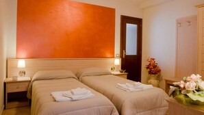 A hotel room with two beds, a large orange accent wall, a wooden wardrobe, and a vase of flowers. - Bed and Breakfast Charme (Sora)